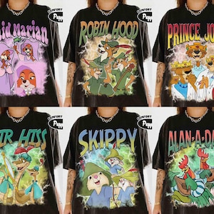 Puede incluir: Camisetas negras con personajes de la película animada "Robin Hood". Cada camiseta muestra un personaje o grupo de personajes diferente con sus nombres en un estilo vintage. Las camisetas tienen un aspecto desgastado.