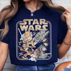 Puede incluir: Camiseta azul marino con un dise&ntilde;o de Star Wars con personajes de Winnie the Pooh. El dise&ntilde;o incluye a Pooh con un sable de luz, Tigger con un blaster y otros personajes con el Halc&oacute;n Milenario. El texto "STAR WARS" est&aacute; en la parte superior.