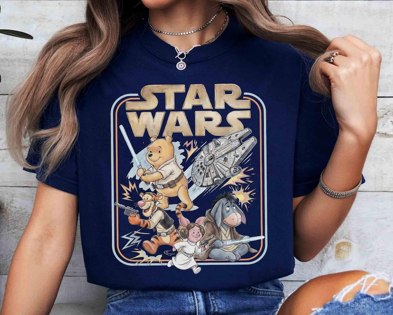 Puede incluir: Camiseta azul marino con un dise&ntilde;o de Star Wars con personajes de Winnie the Pooh. El dise&ntilde;o incluye a Pooh con un sable de luz, Tigger con un blaster y otros personajes con el Halc&oacute;n Milenario. El texto "STAR WARS" est&aacute; en la parte superior.