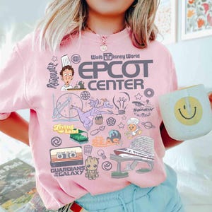 Peut inclure: T-shirt rose clair avec un motif graphique des attractions et personnages d'Epcot Center &agrave; Walt Disney World. Le motif comprend le texte "EPCOT CENTER" et des images de Figment, Remy et les Gardiens de la Galaxie.