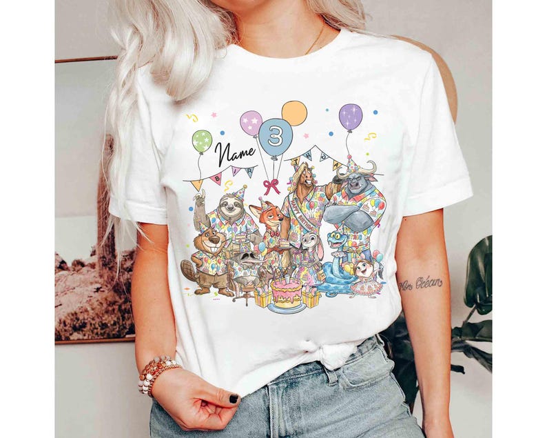 May include: White t-shirt featuring a colorful illustration of cartoon animals celebrating a birthday. The design includes balloons, a cake, and the number 3. The word "Name" is written above the animals.