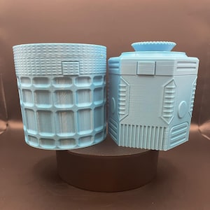 May include: Two light blue plastic containers with different designs. One container is cylindrical with a grid pattern and the other is a cube with a geometric pattern.