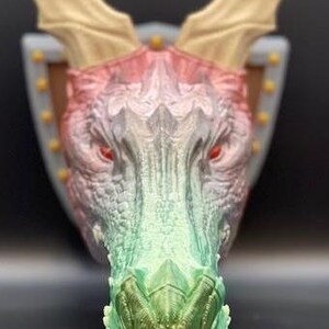 May include: A 3D printed dragon head wall mount with a green, pink and white colour gradient. The dragon has large, pointed ears and a textured snout.