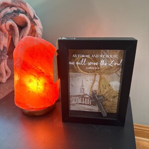 May include: A glowing orange Himalayan salt lamp next to a framed picture with the text "AS FOR ME AND MY HOUSE we will serve the Lord Joshua 24 15". The frame contains a church image and a cross.