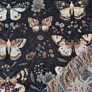 May include: Black woven throw blanket with a colorful fringe. The blanket features a repeating pattern of butterflies and flowers.
