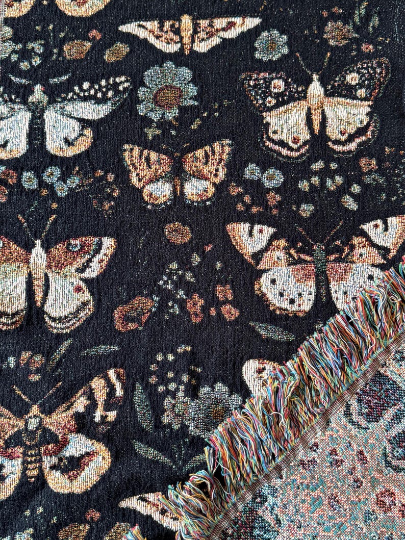 May include: Black woven throw blanket with a colorful fringe. The blanket features a repeating pattern of butterflies and flowers.