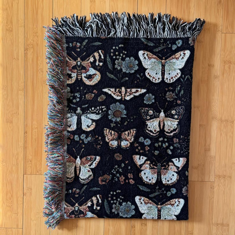 May include: Black woven throw blanket with a fringe border featuring a repeating pattern of butterflies and floral designs.