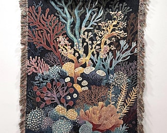 May include: A woven tapestry featuring a colorful coral reef scene with various shades of blue, red, orange, and yellow. The tapestry is framed with a black fringe.