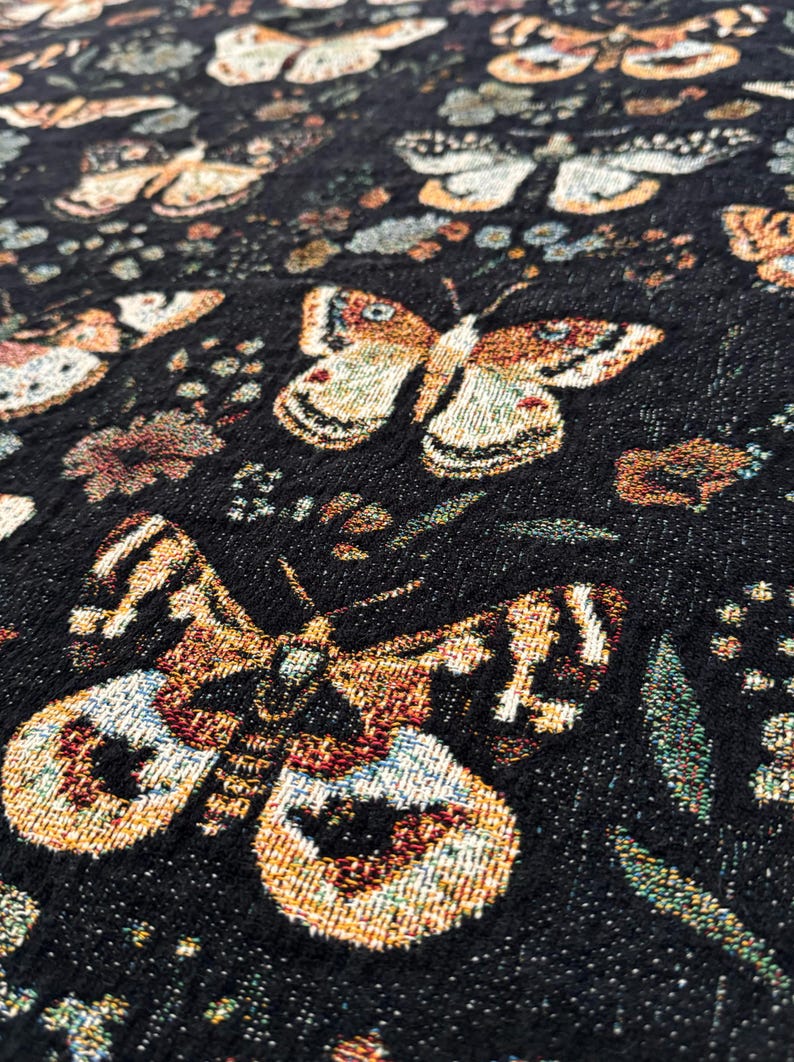 May include: Black fabric with a repeating pattern of gold and brown butterflies and floral designs. The fabric has a textured woven look.
