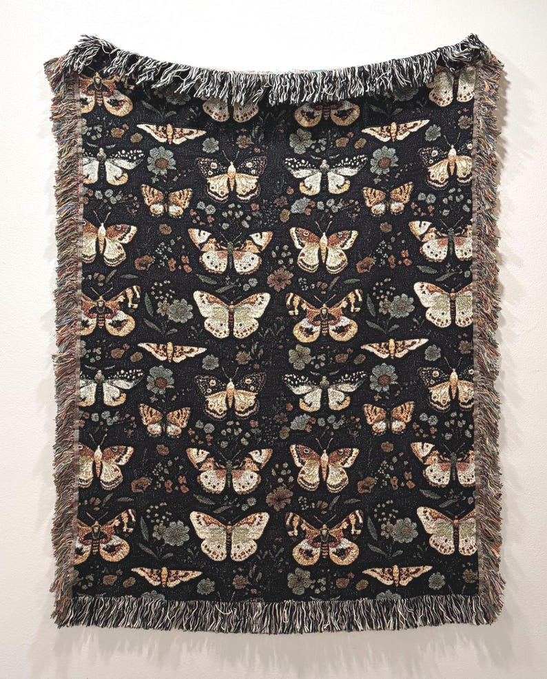 May include: A black woven throw blanket with a repeating pattern of brown and beige butterflies on a dark background. The blanket has a fringe border.