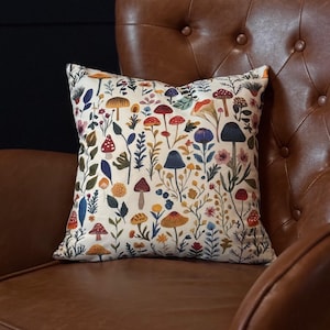 May include: A white cushion with a colourful mushroom and floral pattern. The cushion is sitting on a brown leather armchair.