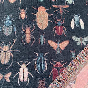 May include: A black woven tapestry with a fringe border features a repeating pattern of colorful insects, including butterflies, beetles, and ladybugs.