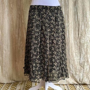 May include: A black and beige floral print skirt. The skirt has a pleated design with a floral pattern and a ruffled hem. The skirt is displayed on a white mannequin.