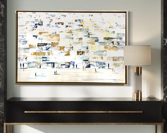 Puede incluir: Pintura abstracta con fondo blanco y formas geométricas doradas, azules y grises. La pintura está enmarcada en oro y cuelga sobre una consola negra.