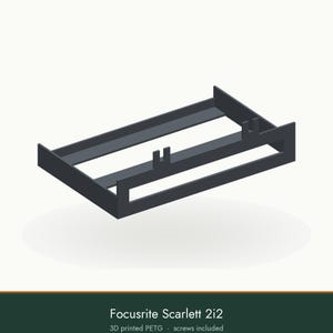 May include: A dark gray 3D printed PETG mounting bracket for a Focusrite Scarlett 2i2 audio interface. The rectangular frame features two vertical support tabs on the top edge and a wide open center design for equipment placement.