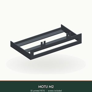 May include: A black 3D printed PETG mounting bracket for a MOTU M2 audio interface. The rectangular frame features two upward-facing U-shaped clips for securing the device. The text MOTU M2 and 3D printed PETG screws included is visible.