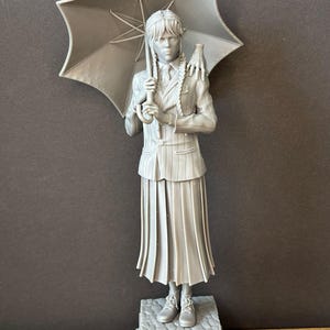 Pode incluir: Uma estatueta cinzenta de uma personagem segurando um guarda-chuva. A figura está vestida com um fato de riscas e uma saia plissada. A base da estatueta diz "WEDNESDAY".