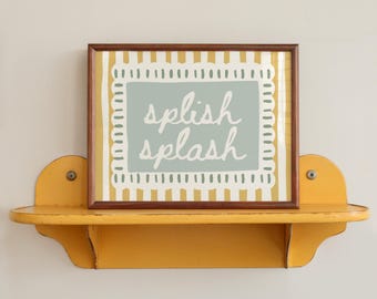 May include: A framed print with the words "splish splash" in a light blue rectangle, set against a yellow and white striped background. The print is displayed on a yellow wooden shelf with decorative brackets.