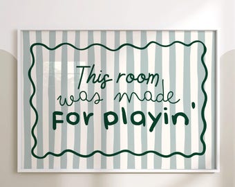 Op de afbeelding: Een ingelijste print met de tekst "This room was made for playin'" in donkergroen schrift. De achtergrond heeft verticale strepen in lichtblauw en wit, omlijst door een golvende donkergroene rand. De lijst is wit.