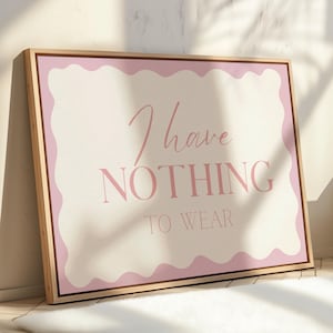 Può includere: Stampa artistica su tela incorniciata con la scritta "I have NOTHING TO WEAR" in rosa. L'opera presenta un bordo ondulato rosa chiaro e uno sfondo color crema, incorniciata in legno naturale.