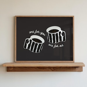 Può includere: Una stampa incorniciata con due tazze di caffè con la scritta "one for you, one for me" in bianco su sfondo nero. Le tazze sono bianche con strisce verticali nere e riempite di caffè scuro. La cornice è in legno marrone chiaro.