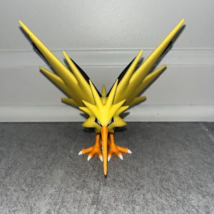 Könnte beinhalten: Eine gelbe Vogelfigur mit schwarzen Akzenten und einem orangefarbenen Schnabel und Füßen. Der Vogel hat große, spitze Flügel und einen strengen Ausdruck. Die Figur ist ein Sammlerstück, wahrscheinlich aus einer beliebten Zeichentrickserie.