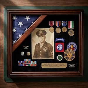 May include: A framed display featuring a folded American flag, a portrait of a U.S. Army officer, and various medals and patches. The display includes the text "AIRBORNE" and "MAJOR JAMES C. CHENAULT. U.S. ARMY".
