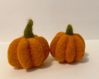 May include: Two small felt pumpkins, one orange and one a slightly darker orange, with green stems.