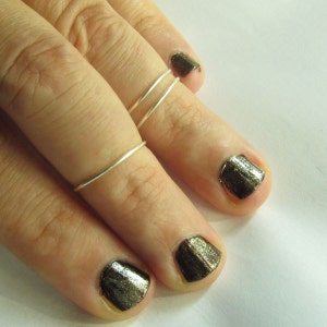 Peut inclure: Une main portant trois bagues fines en argent sur l'index. Les ongles sont peints d'une couleur or métallique foncé.