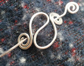 May include: A silver wire hair pin with a spiral design. The pin is on a blue and red fabric background.