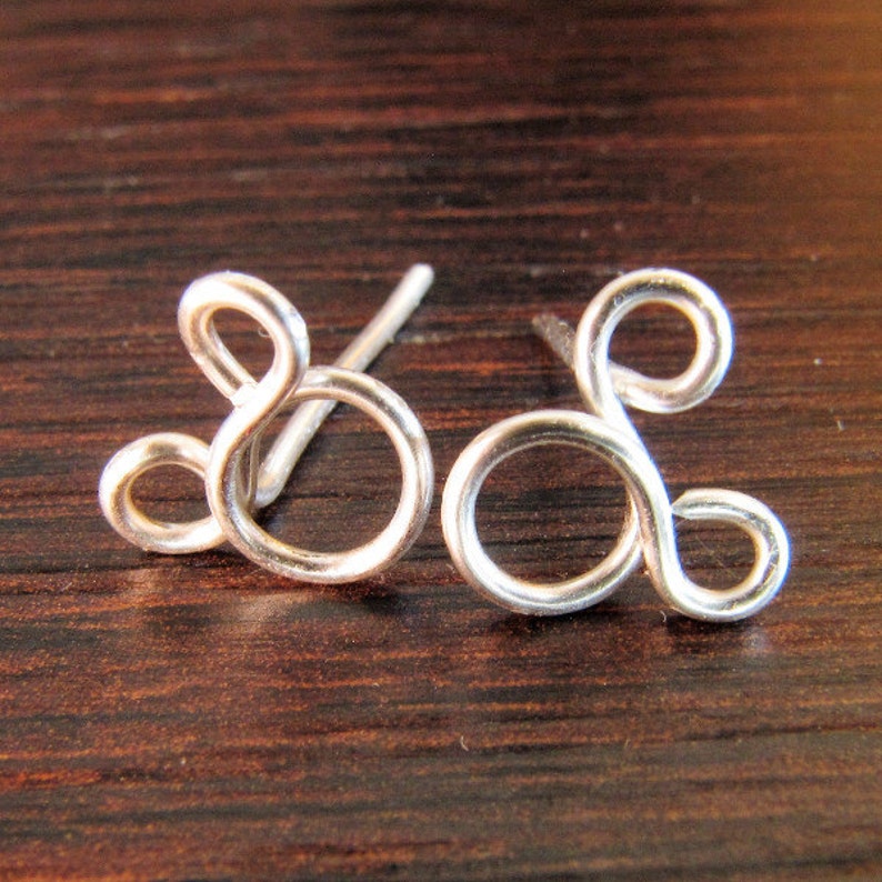 May include: A pair of silver earrings shaped like the infinity symbol. The earrings are made of wire and have a simple, modern design.