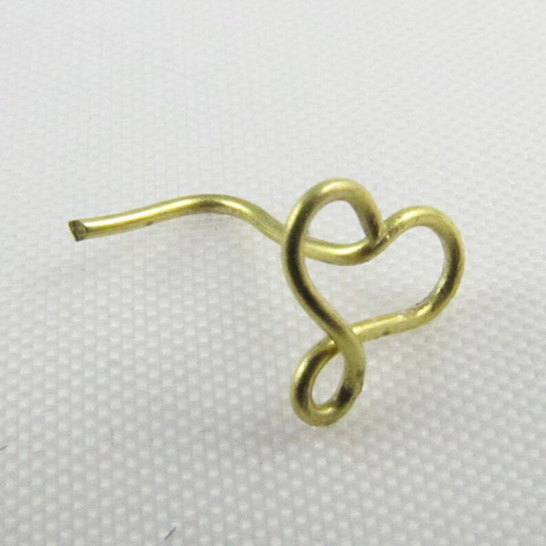 Pu&ograve; includere: Un anello per il naso dorato a forma di cuore con uno stelo curvo.