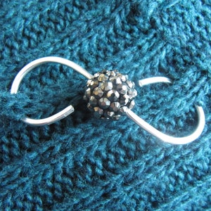 May include: A silver infinity-shaped scarf holder with a black rhinestone accent.