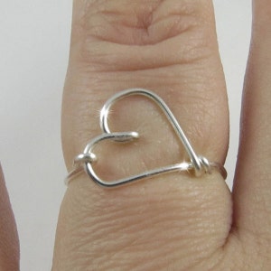 May include: A silver heart-shaped ring, made of wire, worn on a finger.
