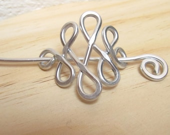 May include: Silver metal hair stick with a decorative knot design. The stick has a spiral end.