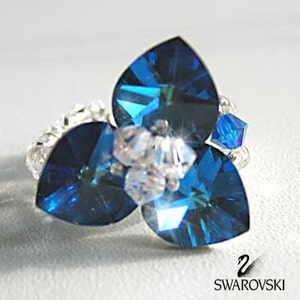 May include: A silver ring with three blue crystal teardrop-shaped stones and a cluster of clear crystals in the center. The ring is made with Swarovski crystals and has the Swarovski logo on the bottom.