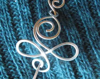 May include: Silver metal hair pin with a swirling design. The pin is on a teal knitted fabric.