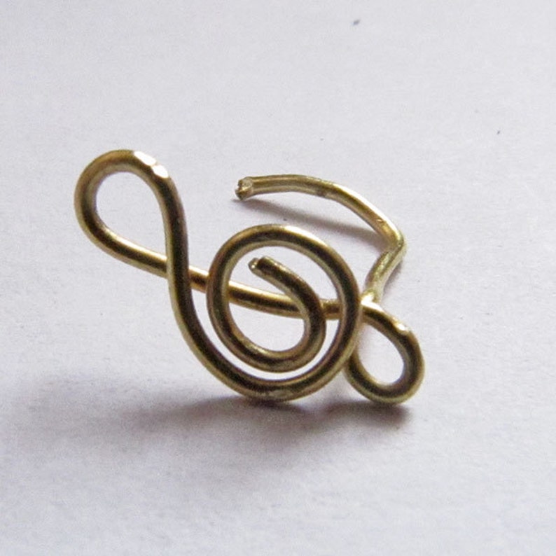 May include: A gold-colored treble clef nose ring. The ring is made of wire and is shaped like a treble clef.