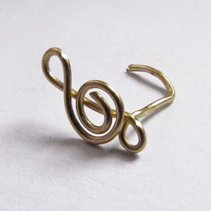 May include: A gold-colored treble clef nose ring. The ring is made of wire and is shaped like a treble clef.