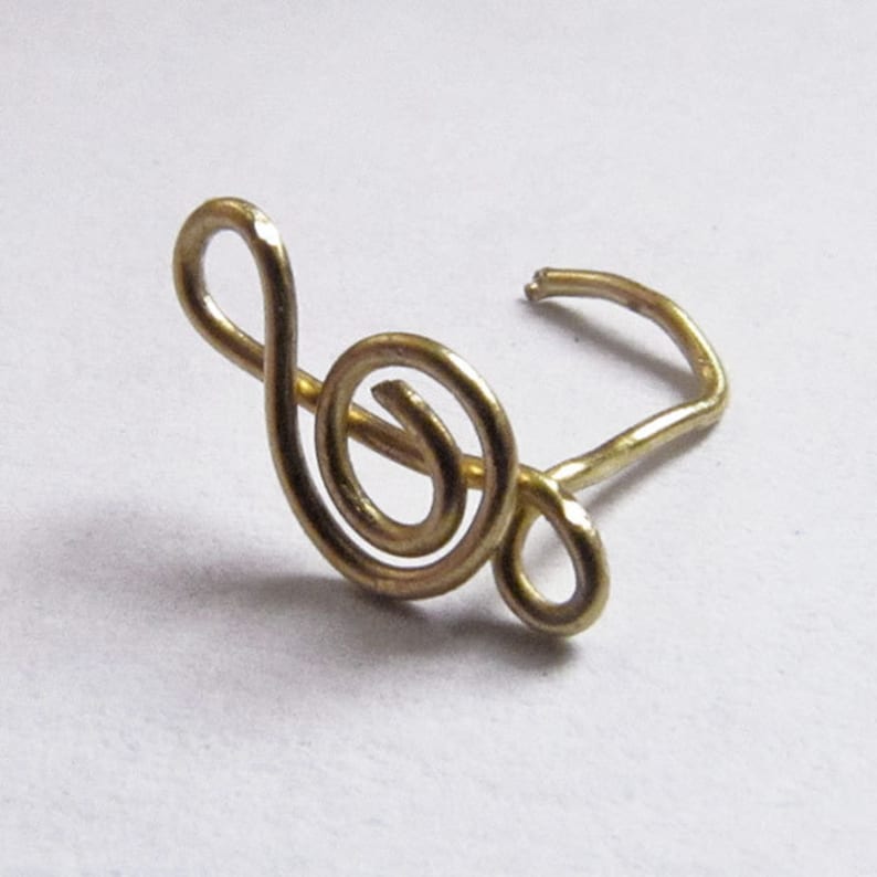May include: A gold-colored treble clef nose ring. The ring is made of wire and is shaped like a treble clef.