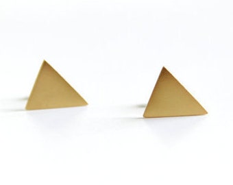 Puede incluir: Un par de pendientes de botón triangulares de color dorado. Los pendientes son formas geométricas simples, cada uno con tres lados y una parte posterior plana para un uso cómodo. Los pendientes se muestran sobre un fondo blanco.