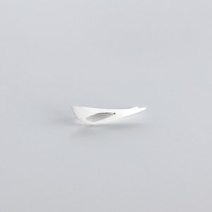 May include: A silver abstract shape brooch with a cutout in the center.