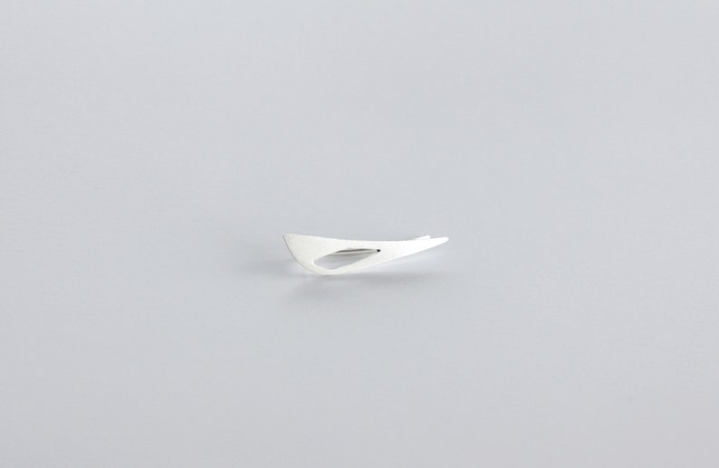 May include: A silver abstract shape brooch with a cutout in the center.