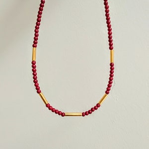 Può includere: Una collana di perline color borgogna con accenti a barra dorata.