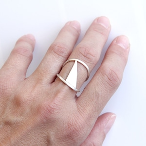 Op de afbeelding: Een zilveren ring met een geometrisch ontwerp. De ring is gemaakt van twee banden die elkaar kruisen om een driehoek te vormen.