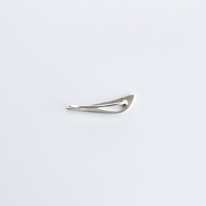 May include: A silver-toned, abstract, geometric shaped brooch. The brooch is shaped like a bird in flight.