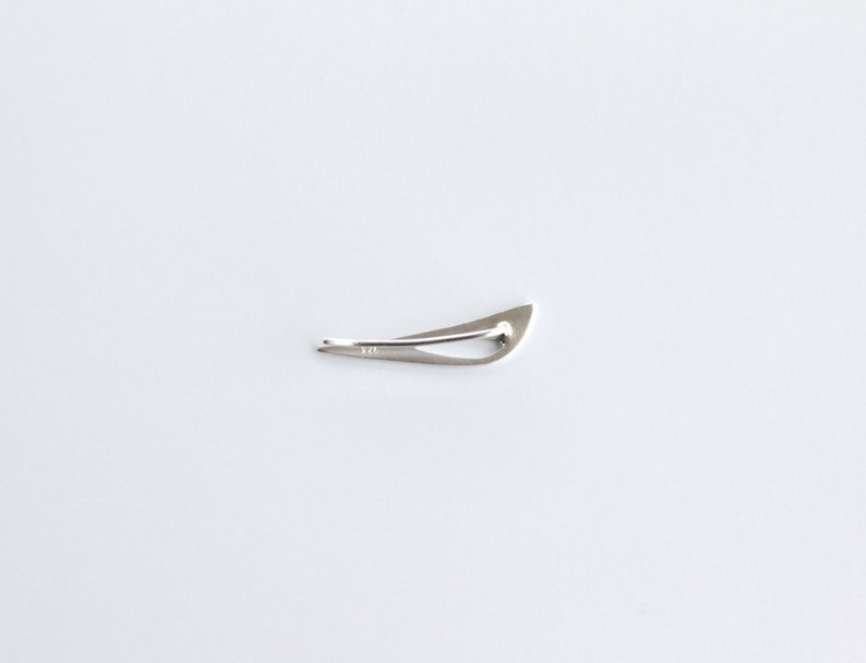 May include: A silver-toned, abstract, geometric shaped brooch. The brooch is shaped like a bird in flight.