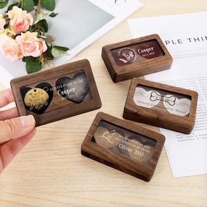 May include: A collection of wooden pet memorial boxes with clear lids. Each box features a decorative element, including metal tags and printed inserts, with text such as "Cooper 2011-2025" and "Forever Loved, Forever Missed".