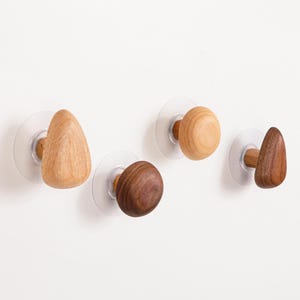 May include: Four wooden wall hooks with varying shapes and wood tones are mounted on clear suction cups. The hooks include a light-colored triangular hook, a round hook, a dark brown spherical hook, and a dark brown triangular hook.