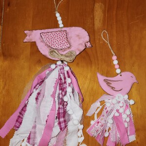 Peut inclure: Deux ornements d'oiseaux roses avec des glands en tissu et des cintres perlés. Les oiseaux ont des ailes à motifs et sont décorés de chutes de tissu, de pompons et de nœuds en ficelle. Ces ornements décoratifs conviennent à la décoration intérieure.